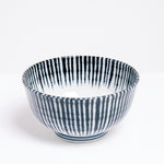 A side view of the white Mino-yaki Tokusa Noodle Bowl on show at NiMi Projects UK. The bowl is made of Japanese porcelain and featuring a traditional pattern of blue stripes representing horsetail grass that extends from its sides over the lip of the bowl to end on the inside in a zigzag pattern.