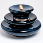 Three blue-glazed ceramic Flat Donut Pedestals — dishes with a central dip and on a raised base — made by artisan Maki Baxter. The three dishes are stacked on top of each other, with the largest at the bottom. 