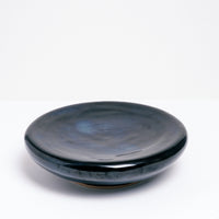 A medium ceramic Flat Donut Pedestal dish, glazed in deep blue, with a central dip and on a raised base. Made by Maki Baxter and available at NiMi Projects UK.