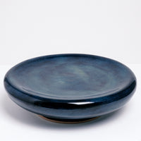 A large ceramic Maki Baxter Flat Donut Pedestal dish on show at NiMi Projects UK. The dish is glazed in deep blue, with a central dip and on a raised base. 