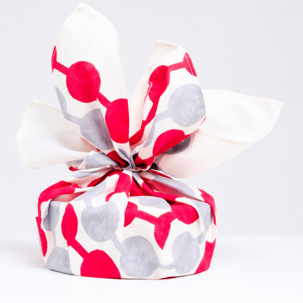A gift wrapped in a Musubi dango furoshiki cloth, featuring lines of dots, alternating in red and grey, designed by Takehisa Yumeji. Available at NiMi Projects UK.