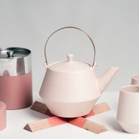 Brass-handled Japanese porcelain Frustum teapot in off white, with matching cups, placed on a pink Sunaolab trivet, available at NiMi Projects in the UK