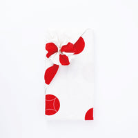 A rectangular box gift wrapped in a Musubi furoshiki Japanese wrapping cloth featuring red dots on a white background.