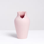 A pink porcelain vase that appears like a figure with a scalloped dress neckline, made by Ceramic Japan and designed by Nendo, displayed on a white background at NiMi Projects UK.