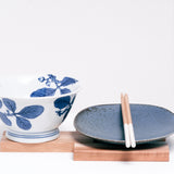 A vintage white Japanese Arita porcelain bowl with a leaf design in blue glaze, a Mino ware porcelain blue plate, and a pair of wooden chopsticks — all displayed on a Tosa Ryu expandable trivet of Hinoki (Japanese Cypress) and Cherry Wood slats. All items from Japan and on show at NiMi Projects UK.