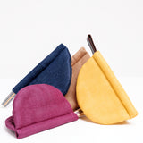 Four different coloured, Japan made, Ban Inoue oven mitts or pot holders, grouped together. Each pot holder is a folded oval shape and stitched in the center - appearing semi circle. Colours clockwise from top left: navy blue, brown, yellow and burgundy. On show at NiMi Projects UK.