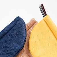 Detail image of the top of three pot holder oven mitts, made in Japan by Ban Inoue. The pot holders are semi-circle, padded and made with a muslin fabric. Colours from left to right: navy blue, brown, yellow. The yellow shows a braided cord for hanging. On show at NiMi Projects UK.