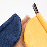 Detail image of the top of three pot holder oven mitts, made in Japan by Ban Inoue. The pot holders are semi-circle, padded and made with a muslin fabric. Colours from left to right: navy blue, brown, yellow. The yellow shows a braided cord for hanging. On show at NiMi Projects UK.