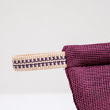 A detail image of the corner of a burgundy  pot holder oven mitt. The mitt is padded and made with muslin and features a braided hanging cord in red and white. Made in Japan and available at NiMi Projects UK.