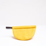 A yellow Ban Inoue pot holder oven mitt. The mitt is lightly padded muslin, oval and folded at the centre to appear semicircle and features a braided hanging cord on the left corner. Made in Japan and on show at NiMi Projects UK.
