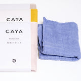 Three Caya muslin kitchen or dish cloths in pink, yellow and beige, each wrapped with a white, paper Caya brand label, fanned out upwards. Next to them is a folded pale blue Caya cloth that has been washed and fluffed. On show at NiMi Projects UK.