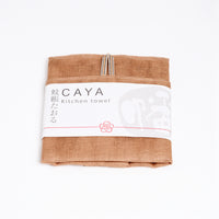 A folded brown yellow Caya kitchen towel, made from Japanese muslin woven using traditional mosquito net weaving techniques. The tea towel is made in Japan by Ban Inoue and wrapped in a white paper label with the Caya logo. Available at NiMi Projects UK.