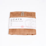 A folded brown yellow Caya kitchen towel, made from Japanese muslin woven using traditional mosquito net weaving techniques. The tea towel is made in Japan by Ban Inoue and wrapped in a white paper label with the Caya logo. Available at NiMi Projects UK.