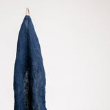 A navy blue Caya kitchen towel, washed and fluffed, hanging from its braided loop. The tea towel is made of Japanese muslin woven using traditional mosquito net techniques. Made by Ban Inoue and available at NiMi Projects UK.