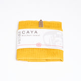 A folded yellow Caya kitchen towel, made from Japanese muslin woven using traditional mosquito net weaving techniques. The tea towel is made in Japan by Ban Inoue and wrapped in a white paper label with the Caya logo. Available at NiMi Projects UK.