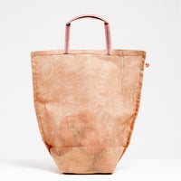 A large brown Ban Inoue Vegetable, slightly transparent tote bag, filled with onions and made in Japan with muslin woven using traditional mosquito net techniques. The bag has a folded and stitched base for support and short top handles. Available at NiMi Projects UK.