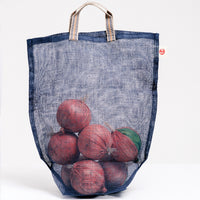 A transparent medium navy blue Ban Inoue Vegetable, filled with several onions and made in Japan with muslin woven using traditional mosquito net techniques. The bag has a folded and stitched base for support and short top handles. Available at NiMi Projects UK.