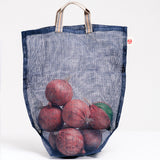 A transparent medium navy blue Ban Inoue Vegetable, filled with several onions and made in Japan with muslin woven using traditional mosquito net techniques. The bag has a folded and stitched base for support and short top handles. Available at NiMi Projects UK.