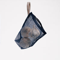 A navy blue, small, transparent vegetable bag. Made in Japan by Ban Inoue using traditional mosquito net weaving techniques. The bag is a rectangle with bottom stitched corners to give it structure. A braided cord at one corner is added to hang it with. On show at NiMi Projects UK.