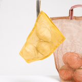 A yellow, small transparent vegetable bag, hanging next to a large version in brown. Both are made by Ban Inoue using traditional mosquito net weaving techniques. Made in Japan, it’s a simple rectangle shape with stitched corners at the bottom for structure. One corner features a braided cord to hang it with. Available at NiMi Projects UK.