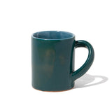 A large deep green glazed ceramic mug with its handle positioned at an angle, designed to make it easier to hold and tilt. Hand made by Angle in Japan and available at NiMi Projects UK.