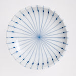 A top view of a white, Japanese porcelain, Mino-yaki pinstriped side dish, showcasing its gently fluted lip and a design of radial thin lines in blue underglaze. Available at NiMi Projects UK.