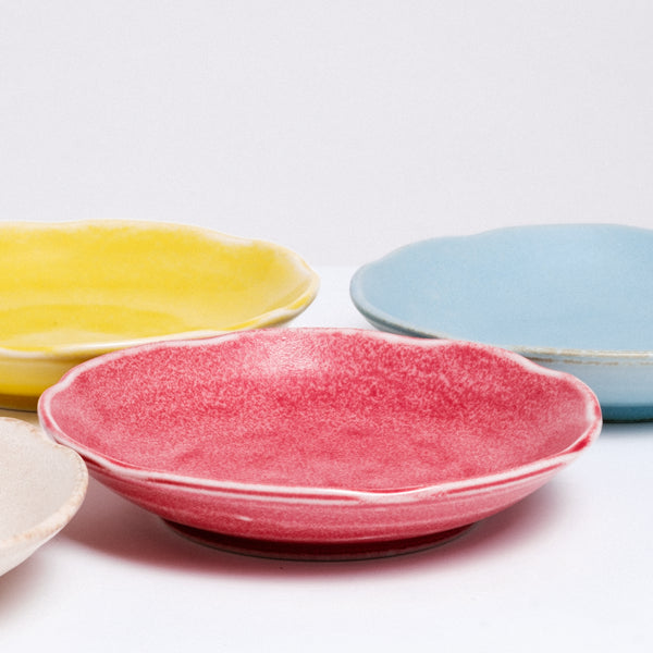 Closeup of four Mino-yaki Japanese porcelain plates with fluted edges available at NiMi Projects. From left to right: Edge of a white plate, a bright yellow plate, a red plate and a sky blue plate.