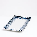 The NiMi Projects’ Mino-Yaki Tokusa Sushi Plate, made of white porcelain and featuring a traditional Japanese horsetail grass pattern of indigo-blue zig-zag stripes that taper inward around the edge like a frame.