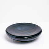 A medium ceramic Flat Donut Pedestal dish, glazed in deep blue, with a central dip and on a raised base. Made by Maki Baxter and available at NiMi Projects UK.