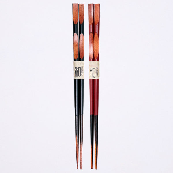 Two sets of natural wood Chopsticks, one pair with black urethane lacquer, the other in red. Both sets have oval shapes carved out at the top and a zig-zag pattern at the bottom to reveal the natural grain of the wood beneath. Available at NiMi Projects UK. 