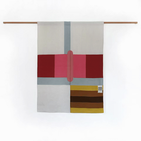 Gif animation of artist and creative director Amy Croft's noren (Japanese curtain) opening and closing on a wooden pole. The curtain is split into two panels, together they create a pattern of red and pink and blue rectangles on a white background, with a central oval pattern in pink and a yellow and brown striped rectangle on the bottom right. Gif and images ©Amy Croft.