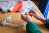 Work in progress image of Amy Croft's hands stitching a Modja Modja House label for her hand-crafted, contemporary Japanese noren. In the background is the unfinished curtain. Image copyright Amy Croft.