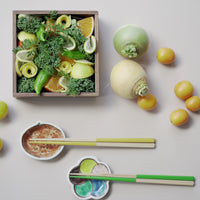Assorted vegetables in a square wooden dish, displayed with turnips and cumquats and two pairs of Style of Japan bicolour chopsticks (yellow and wood, and green and wood), each placed on a small dish, colourful dish.
