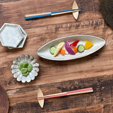 Assorted small, white ceramic dishes with vegetables, all laid out on a wooden table with two pairs of Style of Japan bi-colour Oedo chopsticks — a blue and wood pair at the top, and a pink and wood pair at the bottom.