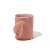 A large pink glazed ceramic mug showing its handle positioned in at an unusual angle to make it easier to hold and tilt. Hand made by Angle in Japan and available at NiMi Projects UK.