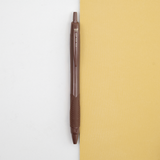 A brown Uniball jetstream retractable pen laid out on a bicolour (white/yellow) background, available at NiMi Projects UK.