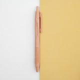 A coral pink Uniball jetstream retractable pen laid out on a bicolour (white/yellow) background, available at NiMi Projects UK.