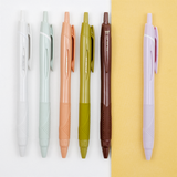 Set of a white, mint green, coral pink, olive green, brown and lilac Uni-ball jetstream gel-ink retractable pens lined up on a bicolour white/yellow background, on show at NiMi Projects UK.