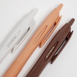 A close up of three different coloured Uniball jetstream retractable pens (white, coral pink and brown) displayed on a white background, available at NiMi Projects UK.