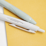 A closeup of mint green and a white Uniball jetstream retractable pen laid out on a bicolour (white/yellow) background, available at NiMi Projects UK.