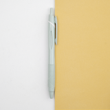 A mint green Uniball jetstream retractable pen laid out on a bicolour (white/yellow) background, available at NiMi Projects UK.