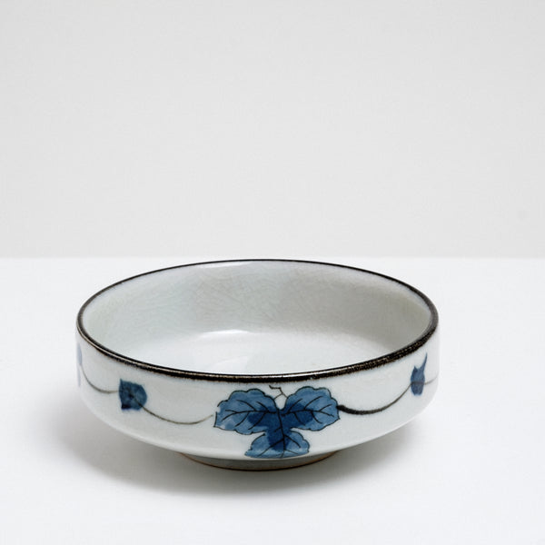 A medium sized Japanese vintage porcelain bowl features a border design of blue underglaze bunches of grapes and grapevine leaves and a crackle glaze.