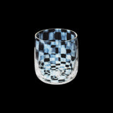 A short, tumbler glass made by Hirota Glass and Moheim, with a rounded base and a pattern of opalescent white and clear checks. Made in Japan and available at NiMi Projects UK.