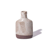 A Japanese ceramic, slim, flat bottle-shaped mini vase with a flecked satin off-white dip glaze and an exposed natural clay. Made by Angle and on show at NiMi Projects UK.