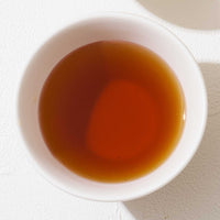 An ariel of a white porcelain cup filled with amber brown Kuan Hojibocha Japanese green tea. ©AWAIDO