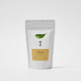 A white pouch of Awaido Japanese green tea leaves. The pouch has a rectangle label with a green illustration of a tea leaf and the name of the tea in Japanese kanji. Below the kanji is an orange section of the label with the name in English: Kuan. Image ©AWAIDO