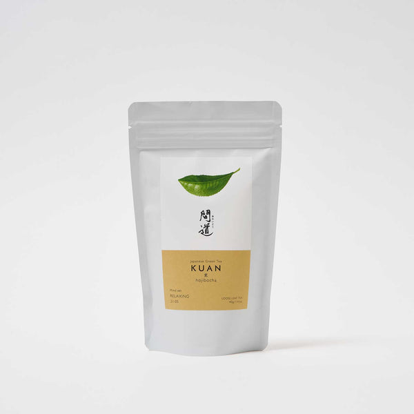 A white pouch of Awaido Japanese green tea leaves. The pouch has a rectangle label with a green illustration of a tea leaf and the name of the tea in Japanese kanji. Below the kanji is an orange section of the label with the name in English: Kuan. Image ©AWAIDO