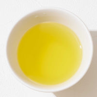 A top view of a white porcelain cup filled with golden, light green Sumi Sencha Japanese green tea. ©AWAIDO