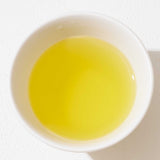 A top view of a white porcelain cup filled with golden, light green Sumi Sencha Japanese green tea. ©AWAIDO