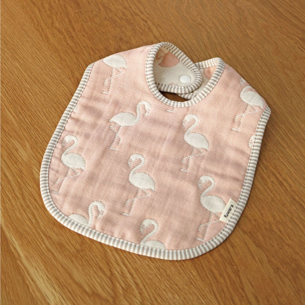 A Fuwara muslin bib made with cotton Japanese gauze in pink, featuring a stitched pattern of white flamingos and grey striped trimming.